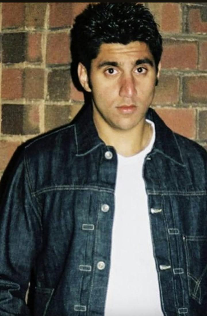 Portrait of Mak Singh in a denim jacket against a brick wall